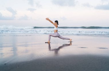 Sahil şeridinde sabah antrenmanı sırasında bacakları ve vücut kaslarını esneten beyaz kadın yogi 'nin yan görüntüsü. Hatha Asana' da deniz kıyısında duran esnek eşofmanlı kadın.