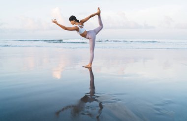 Spor eşofmanlı formalı kız, esneme ve canlandırma için Asana 'yı dengede tutarken bacağını kaldırıyor, Kafkasyalı kadın yoga pozunda uyarak meditasyon yapıyor, hafta sonları antrenman yapıyor.