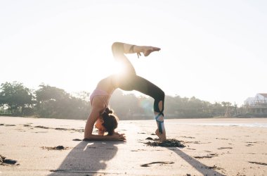 Eşofmanlı sakin, beyaz bir kadın esneme egzersizi yapıyor. Bacağını kaldırıyor ve zayıflatmak için ilham alıyor. Spor yapan kadın antrenör, güneşli sahil şeridinde sabah antrenmanında yoga yapmaktan zevk alıyor.