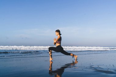 Kafkasyalı genç formda kız gün ışığında deniz kenarında yoga yapıyor. Esnek kadın vücut kaslarını esnetmek için asana yapıyor. Doğada ahenk ve farkındalık hissediyor.