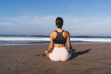 Kıyı şeridindeki Lotus 'ta otururken Zen Bilinci' ni düşünen dişi yogi 'nin arka planda kalan görüntüsü. Sabah antrenmanı sırasında eşofmanlı kadın meditasyon sırasında uyum arayışı için dinleniyor.