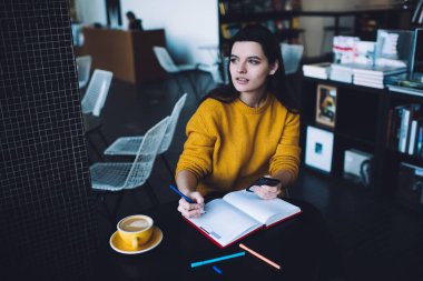Akıllı telefon kullanan ve rahat bir kafede masada otururken not defterine not alan ciddi bir genç bayandan.