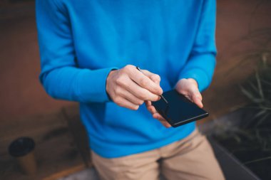 Akıllı telefon aracılığıyla sosyal medya ağı kurarken web içeriği yaratan erkek blogcuya ait kırpılmış görünüm, elektronik stili olan tanınmayan adam online rezervasyon ve bankacılık yapmak için cep telefonu aygıtı kullanıyor