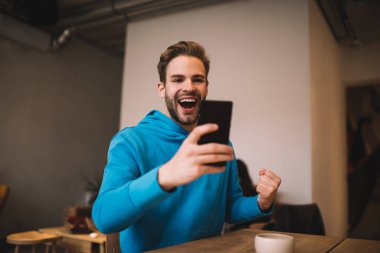 Aşırı neşeli hipster adam, spor bahislerini kazanmaktan mutlu olan e-posta haberlerini okurken seviniyor. Neşeli beyaz blogcu, sosyal ağlarda kendi popülaritesini kutluyor.