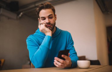 Yakışıklı beyaz tenli hippi kafenin içinde arkadaşını beklerken sıkılıyor. Milenyum erkek blogcusu cep telefonundan içerik yayını okuyor.