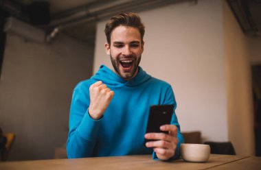 Aşırı neşeli hipster adam, spor bahislerini kazanmaktan mutlu olan e-posta haberlerini okurken seviniyor. Neşeli beyaz blogcu, sosyal ağlarda kendi popülaritesini kutluyor.