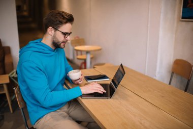Modern dizüstü bilgisayarda web tasarımı konusunda yetenekli beyaz tenli, uzak çalışma sırasında göz koruma programı yaratmak için optik gözlük takan genç bilişim uzmanı