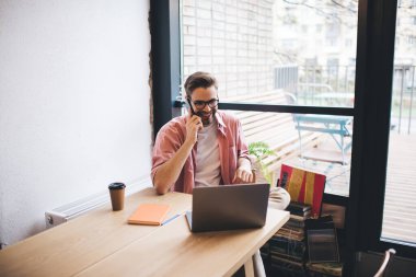 Mutlu erkek serbest çalışan iş arkadaşıyla cep telefonu görüşmesi yapıyor. Uzaktan çalışan neşeli bir adam cep telefonuyla alışveriş yaptığını doğruladı. İnternetten internet üzerinden alışveriş yapıyor.