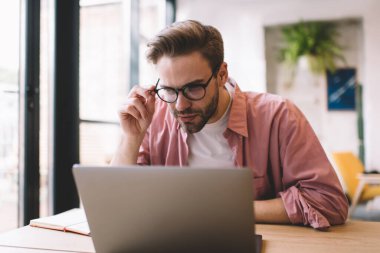 Optik gözlük takan yetenekli hippi adam dijital laptop teknolojisi hakkında bilgi verici web sitesi ile birlikte çalışma alanındaki genel internet bağlantısını kullanıyor, gözlük takan beyaz erkek programcı