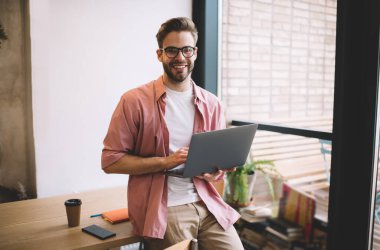 Mola sırasında kameraya gülümseyen dizüstü bilgisayarı olan yarı uzunluktaki neşeli erkek serbest yazar, elinde dijital netbook tutan neşeli Kafkasyalı programcı servis geliştirme için zaman ayırıyor.