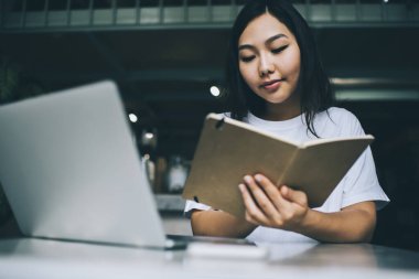 Kafede dizüstü bilgisayarla otururken ve çalışırken not defterinde notlar okurken düşünceli Asyalı serbest çalışan bir kadın.