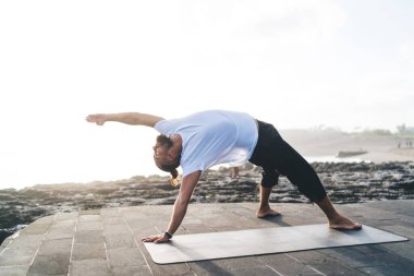 Genç sporcu hafta sonunu Hatha Toprakları 'nda bütünsel iyileşme için harcıyor. Beyaz erkek 20' li yaşlarda Asya 'da meditasyon yaparken deniz kıyısında egzersiz yapıyor.