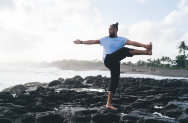 Spor giysilerinde çıplak ayaklı erkek yogi kayalık sahil şeridinde spor yapıyor sağlıklı yaşam tarzını koruyor, beyaz adam yoga pozisyonunda, uyum için meditasyon yapıyor barış dinlenmeye odaklanıyor.