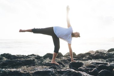 Beyaz erkek sporcu, bacağını kaldırarak yoga yapıyor. Sabahları iç huzuru ve canlılığı hissetmek için poz veriyor. Esnek vücutlu bir erkek Asana 'da fiziksel ve zihinsel sağlığa önem veriyor.