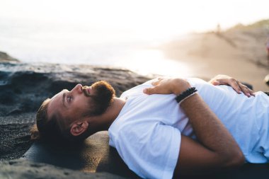 Sakallı, sakallı bir adam. Pranayama yaparken yalan söylüyor ve dinleniyor. Doğal ortamda nefes alıyor.