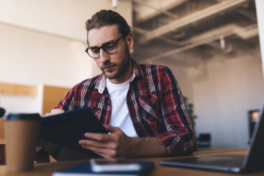 Milenyum Kafkasyalı işadamı panoya bir şey yazıyor ya da bakıyor. Modern başarılı adam kavramı. Gözlüklü genç girişimci açık uzay ofisindeki masada oturuyor ve çalışıyor.