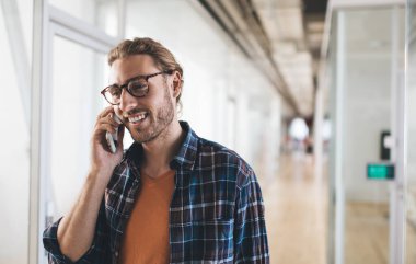Milenyum Kafkas işadamı akıllı telefondan konuşuyor. Modern başarılı adam kavramı. Açık uzay ofisinde çalışan, gözlüklü, gülümseyen genç bir girişimcinin kırpılmış görüntüsü.