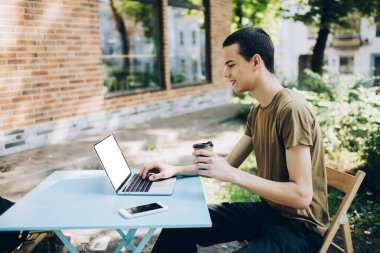Sokakta kahve masasında oturan ve iş sırasında dizüstü bilgisayarla internette sörf yapan pozitif erkek serbest yazar.
