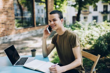 Gülümseyen, dişlek, uzaktan kumandalı neşeli bir erkek. Not defterine not alıp, sokakta cep telefonuyla sohbet ederken başka tarafa bakıyor.