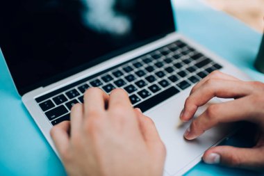 Yüksek ekin açılı, isimsiz bir erkek uzaktan kumandalı işçi masada oturuyor ve modern dizüstü bilgisayarda iş yaparken internette sörf yapıyor.