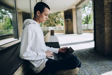 Şehir sokaklarında çalışırken rahat poz veren ve internette gezinen düşünceli serbest çalışan erkek.