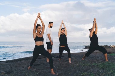 Bir grup esnek erkek ve kadın hatha asana ile birlikte kıyı şeridi sahilinde meditasyon yaparlar, eşofmanlı sporcular deniz kıyısında sabah yoga eğitimi alırlar zen farkındalığı üzerine yoğunlaşırlar.