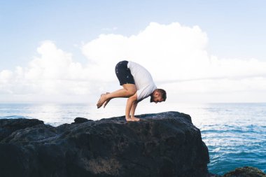 Yogayı dengelemek için pompalanan erkek yoganın yan görünüşü iç huzuru ve el canlılığını hissetmek, Asya 'da ayakta duran güçlü vücutlu erkek deniz kıyısındaki fiziksel ve zihinsel sağlığı önemsiyor.