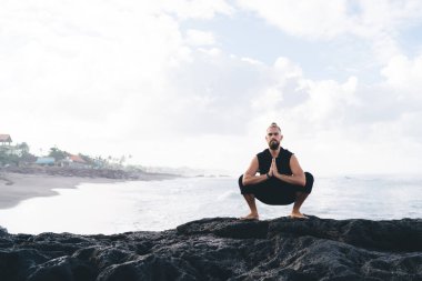 Spor dalında yakışıklı beyaz yogilerin portresi kıyı şeridi antrenmanı sırasında kameraya bakıyor zihin konsantrasyonu için genç bir erkek namaste meditasyonu sırasında dua ediyor.