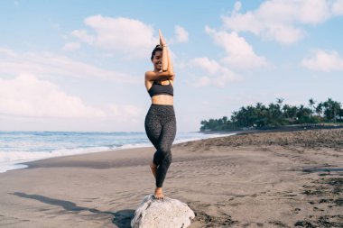 Asya 'daki neşeli zinde kız sabah yoga yaparken mutluluk ve uyumu hisseder kıyı şeridinde meditasyon yaparken, eşofmanlı neşeli bir kadın deniz kıyısında canlılık ve sağlık eğitimi alırken sevinir.