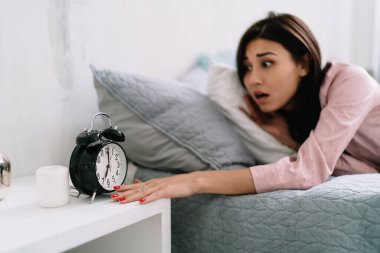 Genç, korkmuş Asyalı kadın sabah vakti yatakta uyuduktan sonra çalar saatin çalmasını bekliyor. Ev hayatı kavramı. Evde dinlenme fikri var. Pijama giyen esmer kız. Modern geniş yatak odası