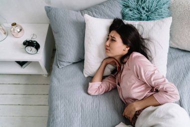 Genç, tatminsiz Asyalı bir kadının sabahları uyuduktan sonra çalar saate baktığı en iyi manzara. Ev hayatı kavramı. Evde dinlenme fikri var. Pijama giyen esmer kız. Modern daire