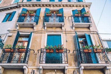 İtalya 'da yaz günlerinde mavi pencereli antik evlere ve çiçek saksılarıyla süslü balkona bakan Venedik mimari binaları şehir turu sırasında görülmeye değer.