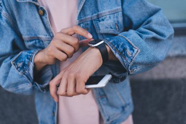 Cep telefonu okuyan kesilen erkek turist dijital kol saati ile tebligat aldı, kot ceketli tanınmayan hipster blog yazarı giyilebilir akıllı ayakkabı teknolojisini kontrol ediyor.