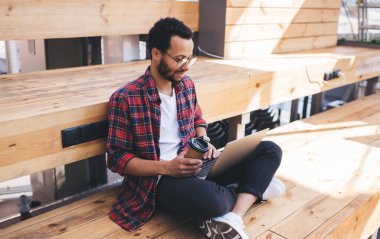 Milenyum erkek blogcusu, gözlükleriyle sosyal ağlarda medyayı tarıyor, dizüstü bilgisayarını kullanıyor, kahveyle yetenekli hipster adam dijital netbook üzerinden online iletişim kuruyor.