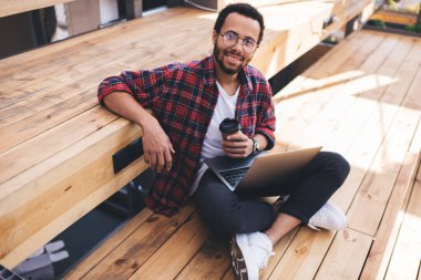 Kahveli yakışıklı İspanyol web programcısının portresi ve birlikte çalışma mesafesinde bilgisayara gülümseyen dizüstü bilgisayar netbook ve paket servis kupası ile birlikte gelişen mutlu erkek IT uzmanı.