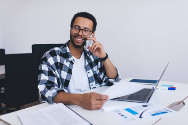 Rapor belgelerine ve laptop teknolojisine sahip mutlu İspanyol çalışanı cep telefonu aygıtını kullanarak iş fikirlerini tartışıyor, neşeli yönetici çalışma sürecinden bahsediyor.