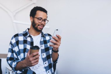 Cep telefonu uygulaması kullanan klasik göz giysisi giyen bin yıllık erkek ve akıllı telefon zımbırtısıyla mesajlaşmak için 4G kablosuz bağlantı kuran genç hippi kahve molasında internet ağında e-posta okuyordu.