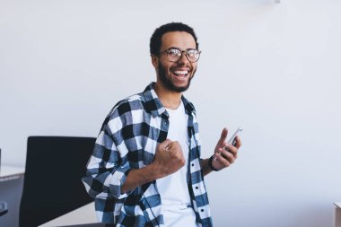 Optik gözlüklü neşeli hippi iş fırsatları hakkında mobil haberler aldı. Akıllı telefon taraması sırasında gözlüklü heyecanlı bir erkek çalışanı online hedefi kutluyor.