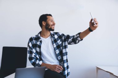 Akıllı telefon cihazıyla selfie çekerken gülümseyen neşeli genç adam, mutlu hipster blogcu cep telefonuyla 4G kablosuz interneti bağlayan arkadaşça görüntülü sohbetin keyfini çıkarıyor.