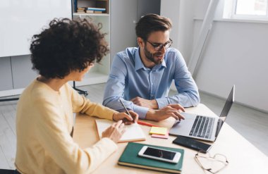 Dizüstü bilgisayardan bir şey izleyen erkek meslektaşına gülen bir iş kadını. İş birliği ve takım çalışması. Genç Kafkasyalı milenyum insanları ofiste masa başında. Modern başarılı insanlar