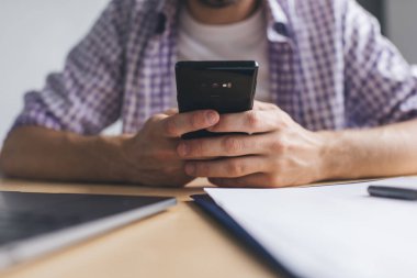 Milenyum işadamının iş sırasında akıllı telefondan mesaj atarken kısmi görüntüsü. Modern başarılı adam kavramı. Tahta masada dizüstü bilgisayarı ve kaydıyla oturan adam.