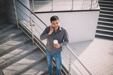 Asyalı milenyum çocuğu ofis binasının yanındaki merdivenlerde akıllı telefondan konuşuyor. Dinlenme ve işten ayrılma kavramı. Modern, başarılı bir adamın fikri. Kahveli genç bir erkek başka tarafa bakıyor. Güneşli bir gün
