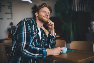 Kafkasyalı düşünceli bir adam çay ya da kahve içiyor ve ofis alanına bakıyor. Dinlenme ve işten ayrılma kavramı. Modern, başarılı bir adamın fikri. Akıllı telefonlu genç bir adam masada oturuyor.