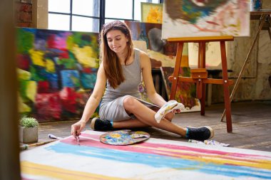 Beyaz kadın resim çizimi yapmak için paletteknife kullanıyor. Sanat stüdyosunda yerde dinlenirken. Paletli genç yetenekli amatör, hafta sonu hobileriyle vakit geçirmek için dinleniyor.