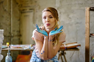 Hafta sonu atölyesinde renkli elleri olan oyuncu amatör kadın ressamlar başyapıt yaratmak için çalışırken sana öpücük yollayan sıradan kıyafetli güzel kadın portresi.