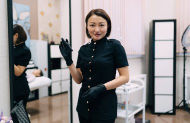 Kaş makyajı için iğne aletli kadın güzellik uzmanının ön görüntüsü ya da kameraya bakan mikroplar. Yetişkin Asyalı kadın üstat eldiven giyiyor. Güzellik konsepti. Modern güzellik salonunun içi.