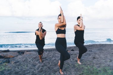 Esnek erkek ve kadınlar sabah kıyı şeridinde antrenman yaparken Asana 'da nefes alıyor, sakin sportif insanlar formda ve sağlıklı bir yaşam tarzıyla yoga yapıyor ve plajda egzersiz yapıyor.