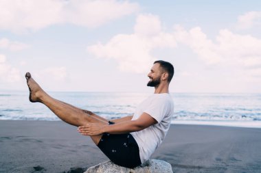 Kafkas erkek yogi vücut dengesi ve deniz kıyısındaki bütünsel iyileşme süresince konsantrasyon eğitiminin yan görüntüsü. Spor giyim kuşağında genç bir adam gündüz vakti doğada kaslarını esnetiyor.