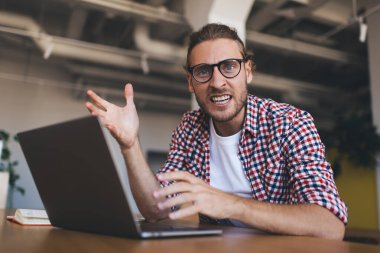 Optik gözlüklü kızgın bir bilişim uzmanının portresi kızgın bir şekilde kameraya bakıyor. Uzaktan kumandanın dizüstü bilgisayarda çalışmasıyla ilgili sorunları var. Fazla mesai programında mutsuz bir programcı.