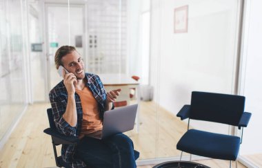 Netbook sistemini tartışırken gülümseyen neşeli programcı, dijital dizüstü bilgisayarı olan mutlu beyaz erkek bilişim uzmanı akıllı telefon uygulaması kullanarak